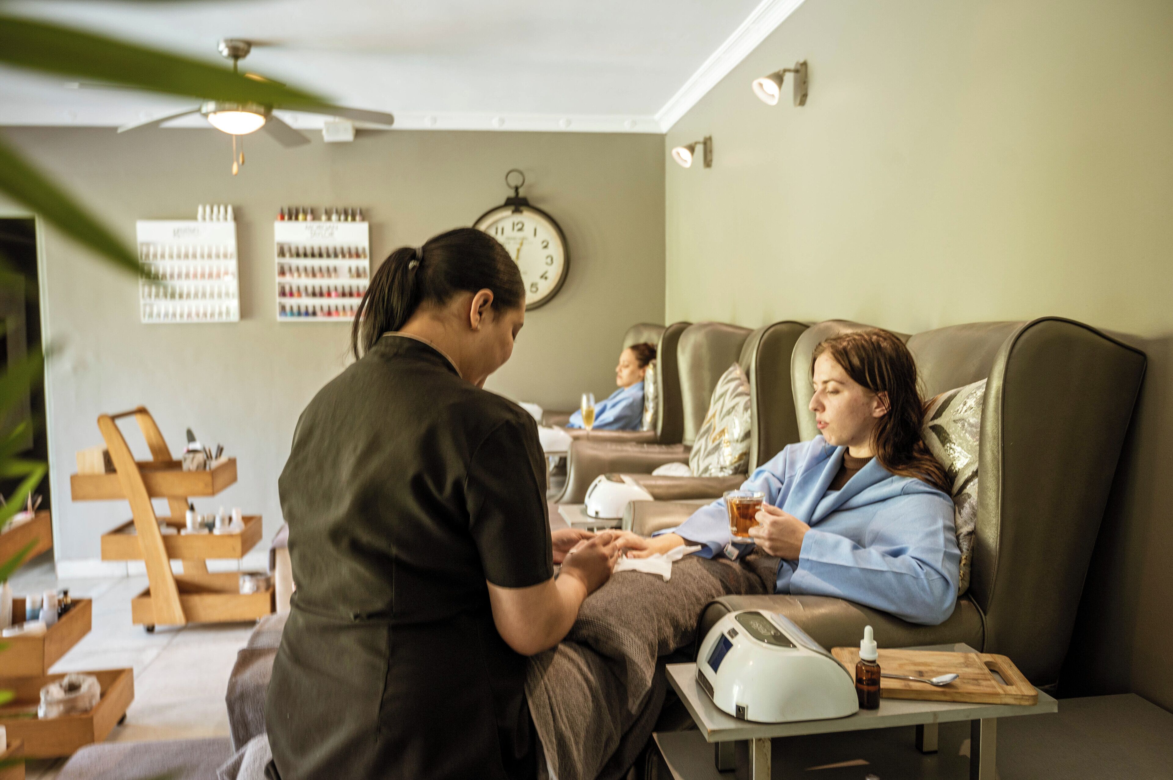 A salon with a massage chair, a clock on the wall, and a shelf with bottles.