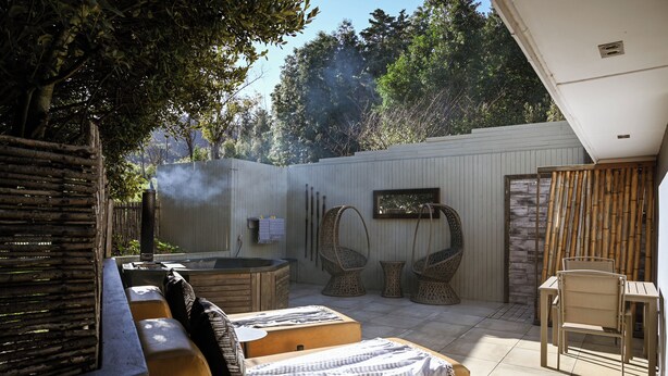 A sunlit outdoor patio with a sofa, two wicker chairs, a small table, and a hot tub. - Silver Forest Boutique Hotel, Spa, Restaurant & Bar (Cape Town)