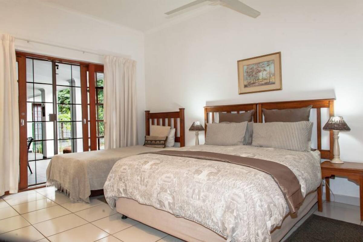 A bedroom with a double bed, a chair, a nightstand, a lamp, and a window with curtains.