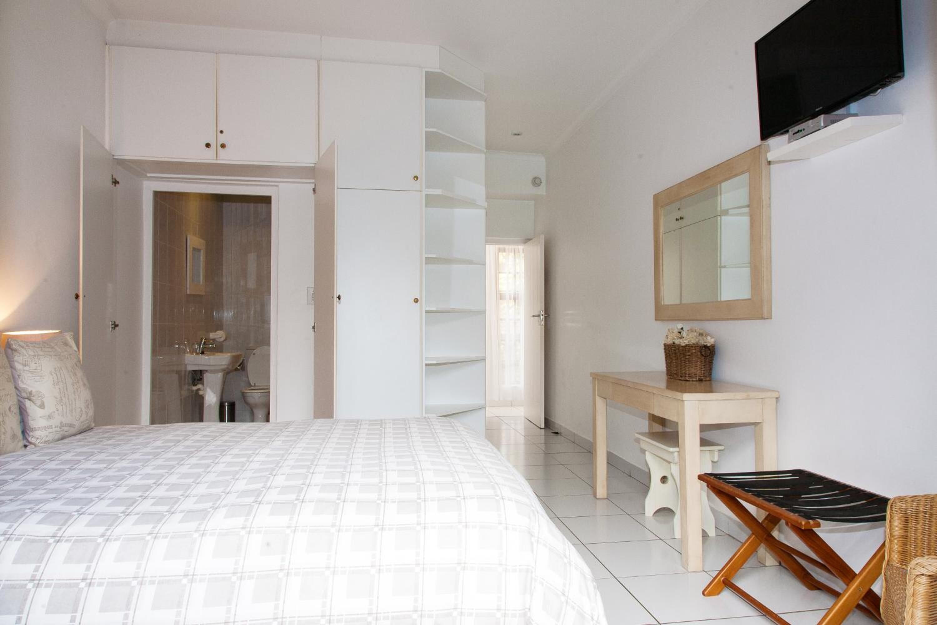 A bedroom with a bed, a desk, a chair, a TV, and a wardrobe.