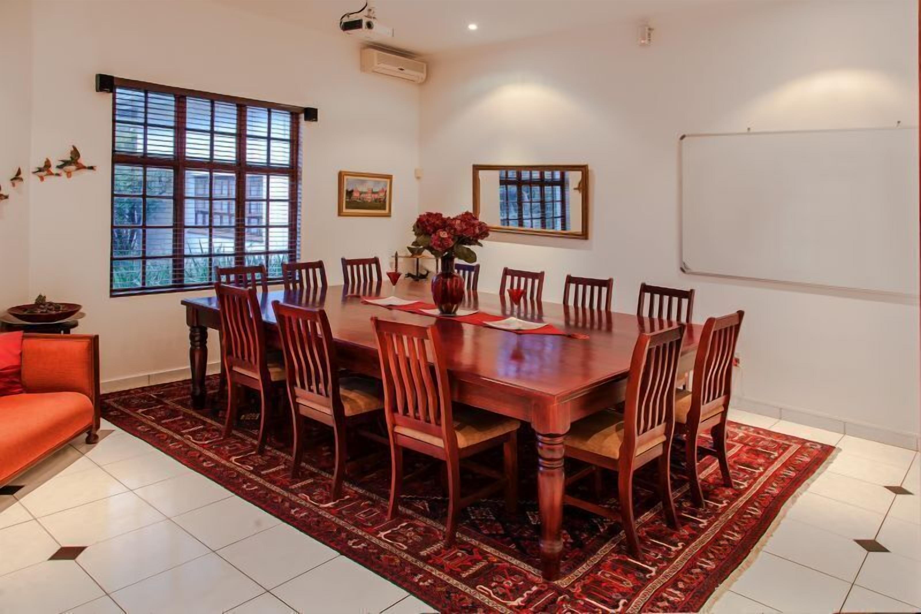 A dining room with a large wooden table, eight chairs, a vase with flowers, and a red sofa.