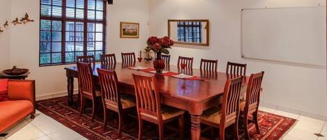 A dining room with a large wooden table, eight chairs, a vase with flowers, and a red sofa.