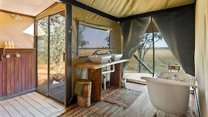 Une pièce aménagée comme une tente, avec un plancher en bois, une grande fenêtre, un lavabo, une baignoire et un meuble en bois.