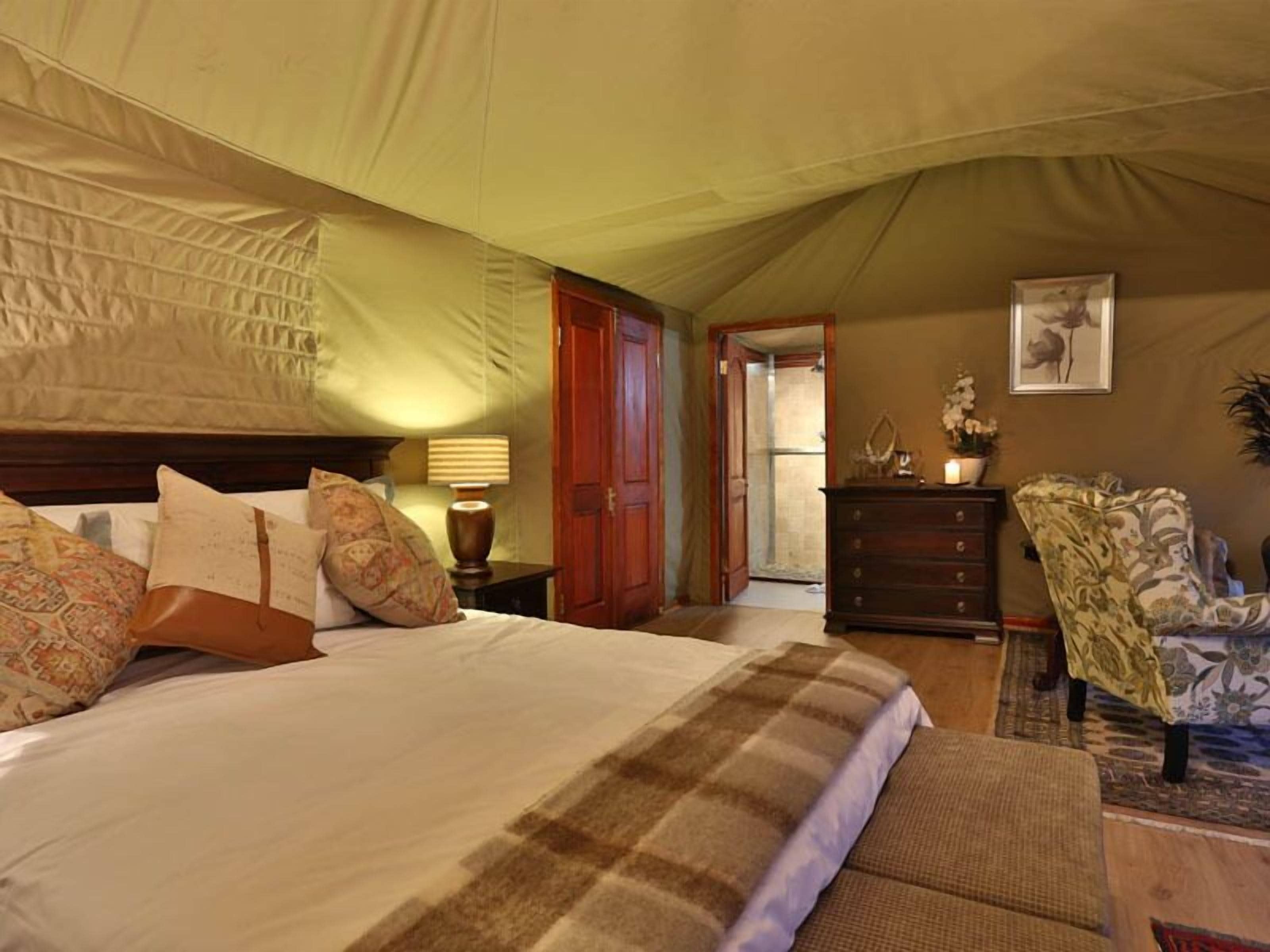 A bedroom with a large bed, a wooden dresser, a chair, and a lamp.
