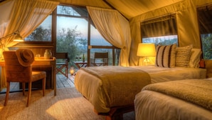 Une chambre confortable, aménagée comme une tente, avec un lit, une chaise, une table et une vue sur l’extérieur.