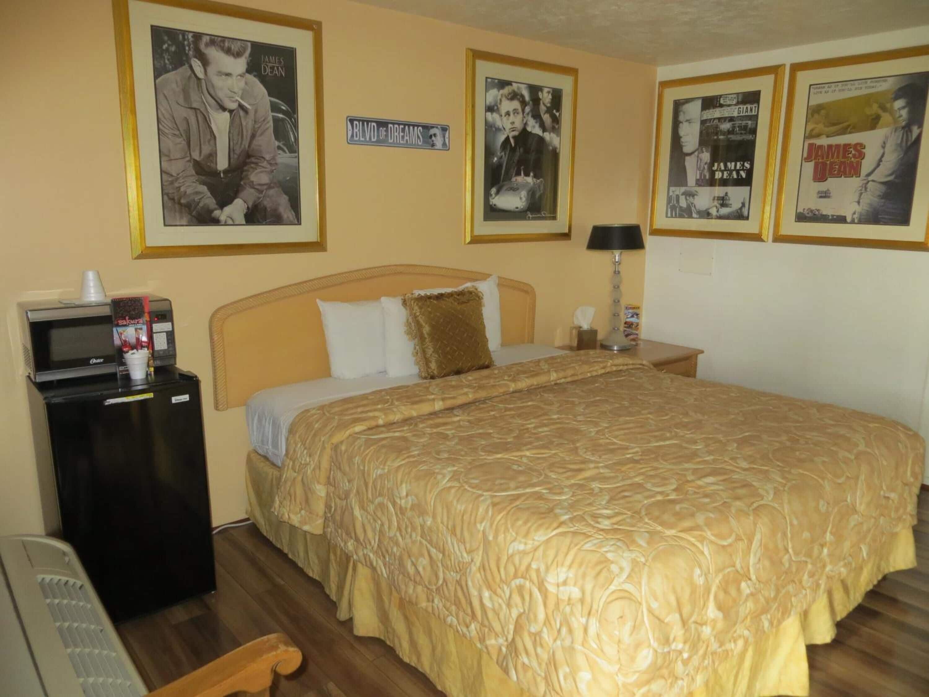 A hotel room with a bed, a desk with a microwave, and framed posters on the wall.