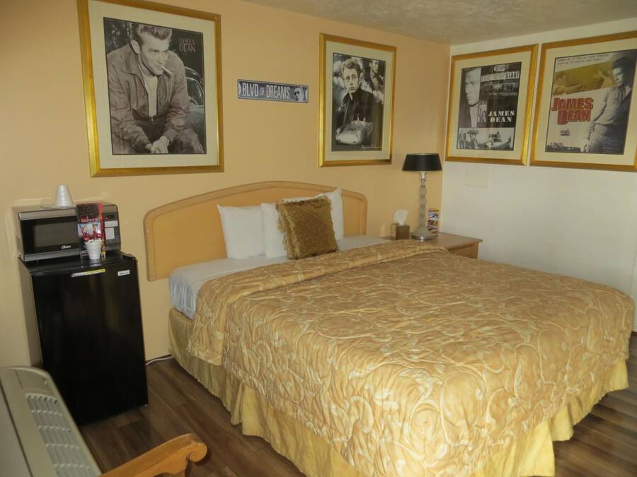 A hotel room with a bed, a desk with a microwave, and framed posters on the wall.