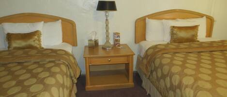 Una habitación de hotel con dos camas, cada una con cabecero, mesita de noche con lámpara y un cuadro enmarcado en la pared.