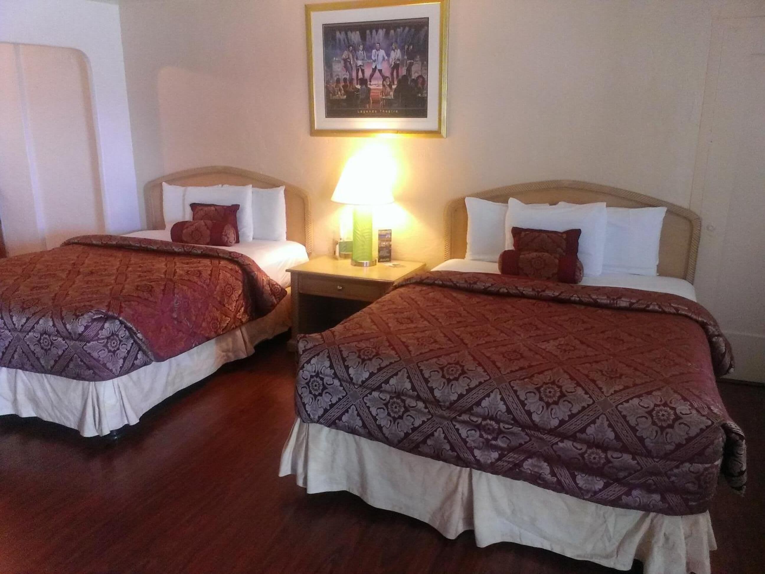 Habitación de hotel con dos camas, cada una con una colcha estampada, una mesita de noche con lámpara y un cuadro enmarcado en la pared.