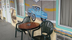 A building exterior with Route 66 painted on the wall, a blue car mural, and a small outdoor seating area with two chairs and a table. - El Trovatore Motel (Kingman)