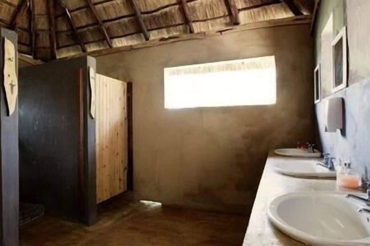 A rustic bathroom with wooden walls, a thatched roof, and a window providing natural light.