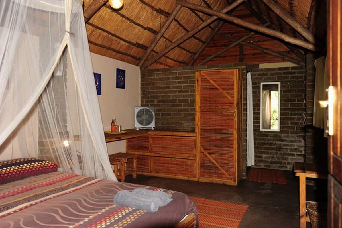 A bedroom with a bed, a mosquito net, a fan, and a brick wall.