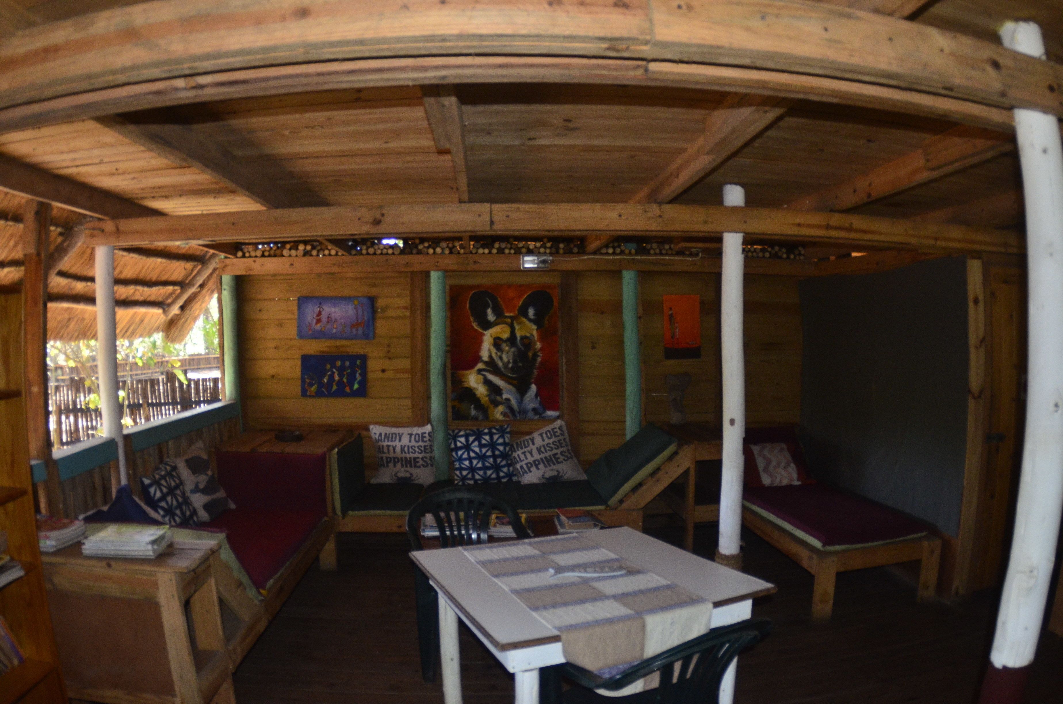 A cozy wooden cabin with a curved ceiling, a central seating area with cushions, a table, and a bed.