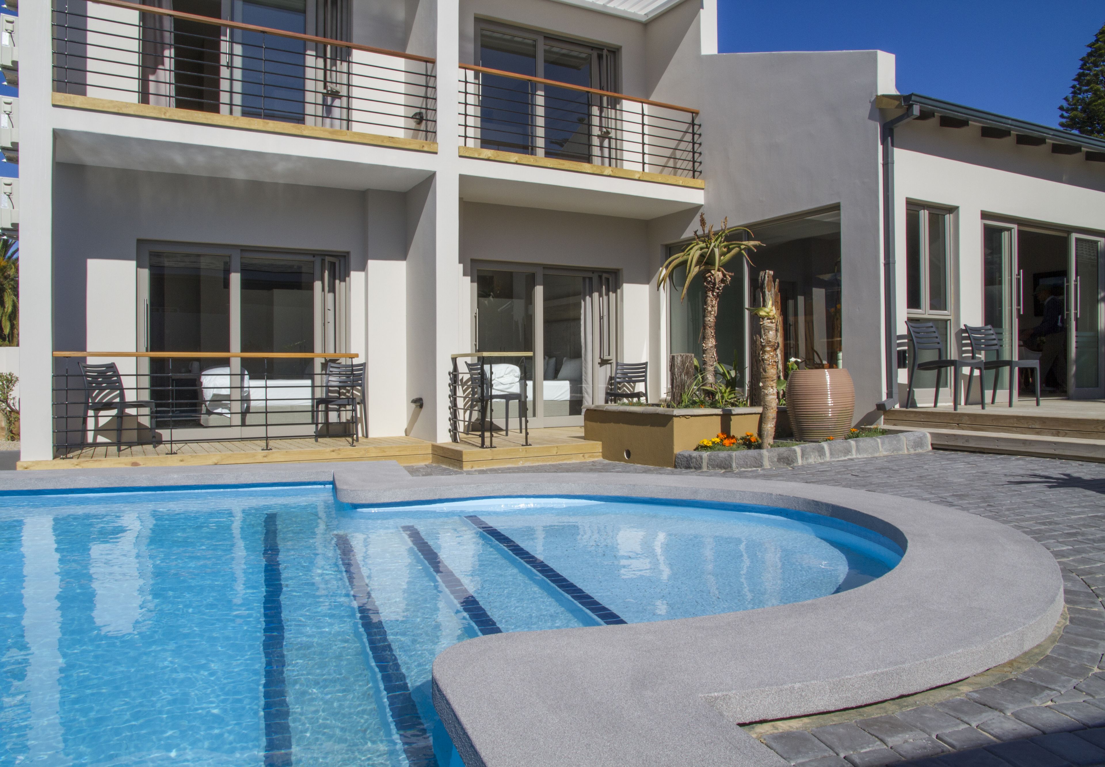 Un edificio moderno con piscina, mobiliario exterior y balcón.