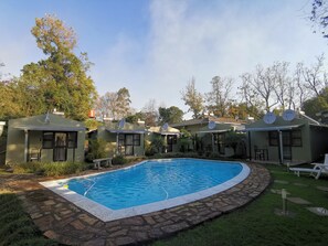 A pool area with a stone border, surrounded by small houses with satellite dishes. - The Place Guest House (Mbabane)