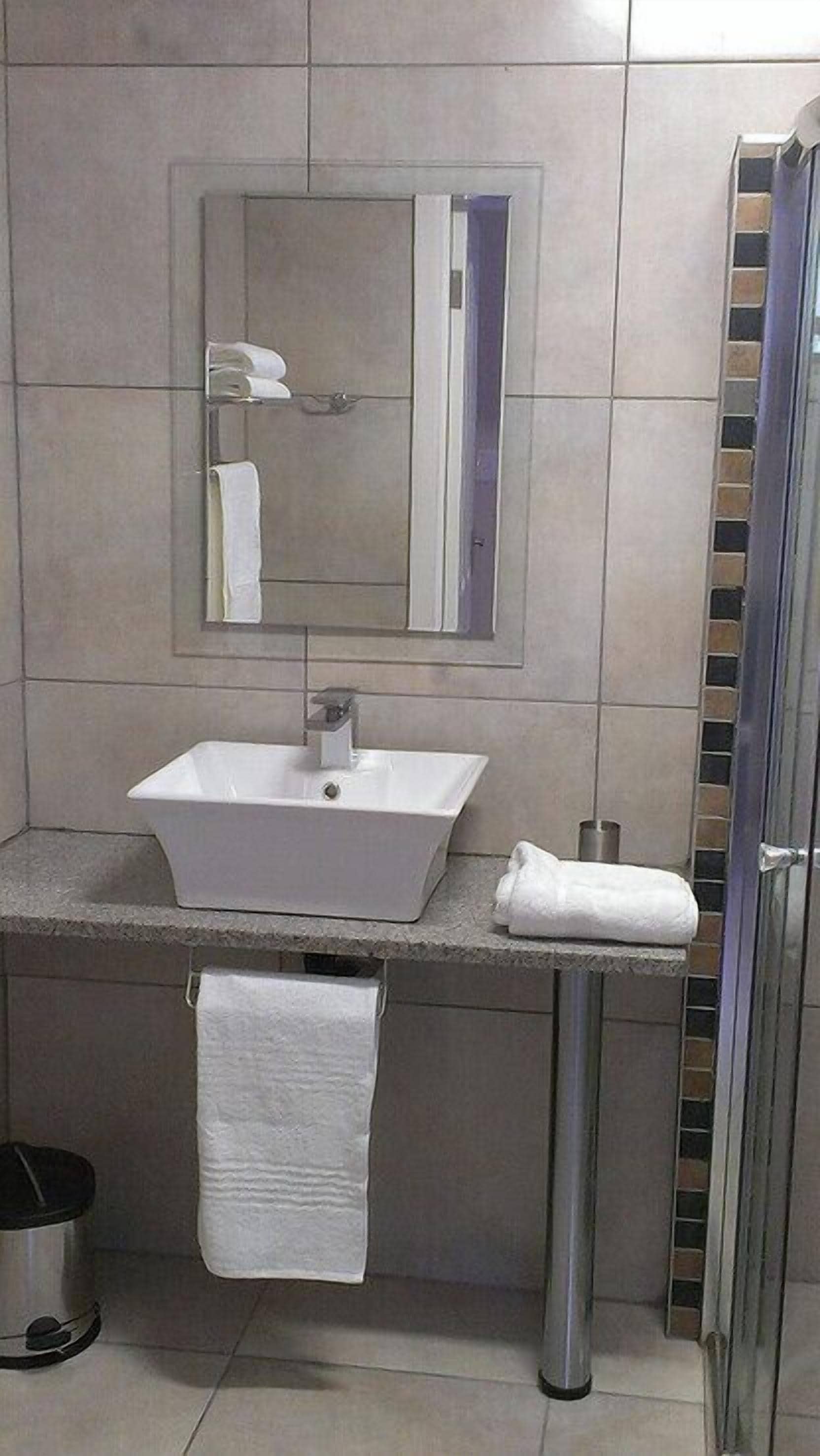 Ein Badezimmer mit einem weißen Waschbecken, einem Spiegel und einem Handtuchhalter.