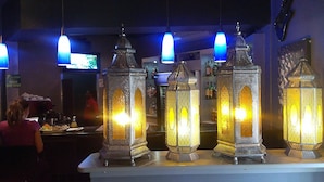 L’intérieur d’un restaurant, avec de somptueuses lanternes en métal sur le comptoir et des suspensions bleues au-dessus.