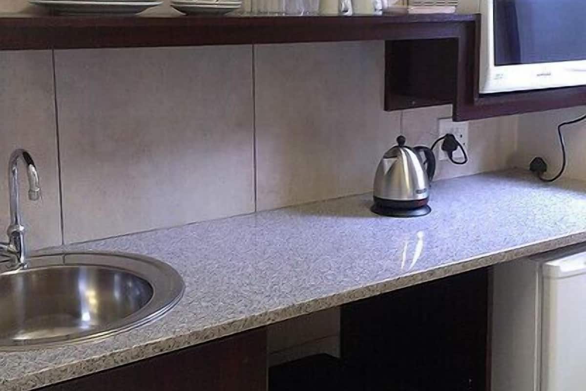 A compact kitchen with a built-in sink, a microwave, and a kettle on the countertop.