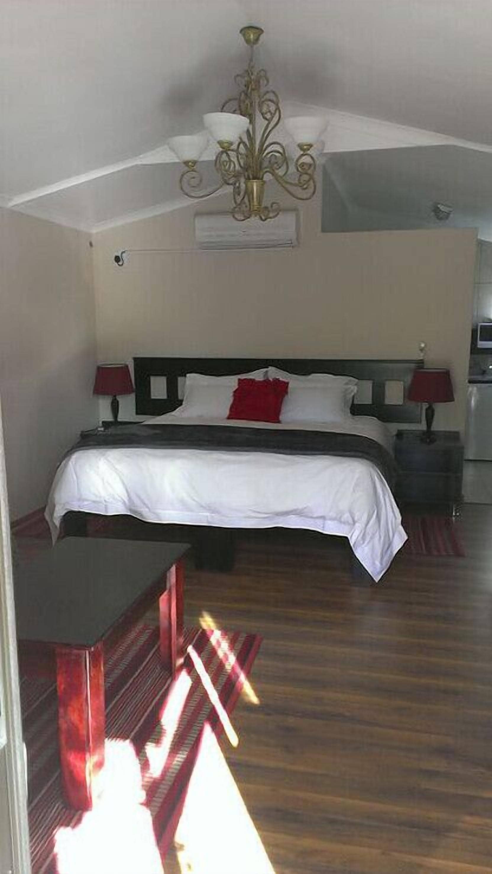 A bedroom with a bed, bedside lamps, a chandelier, and a wooden floor.