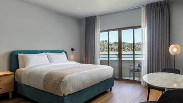 Une chambre d’hôtel moderne avec un grand lit, un balcon offrant une vue agréable, une table à manger et une lampe.