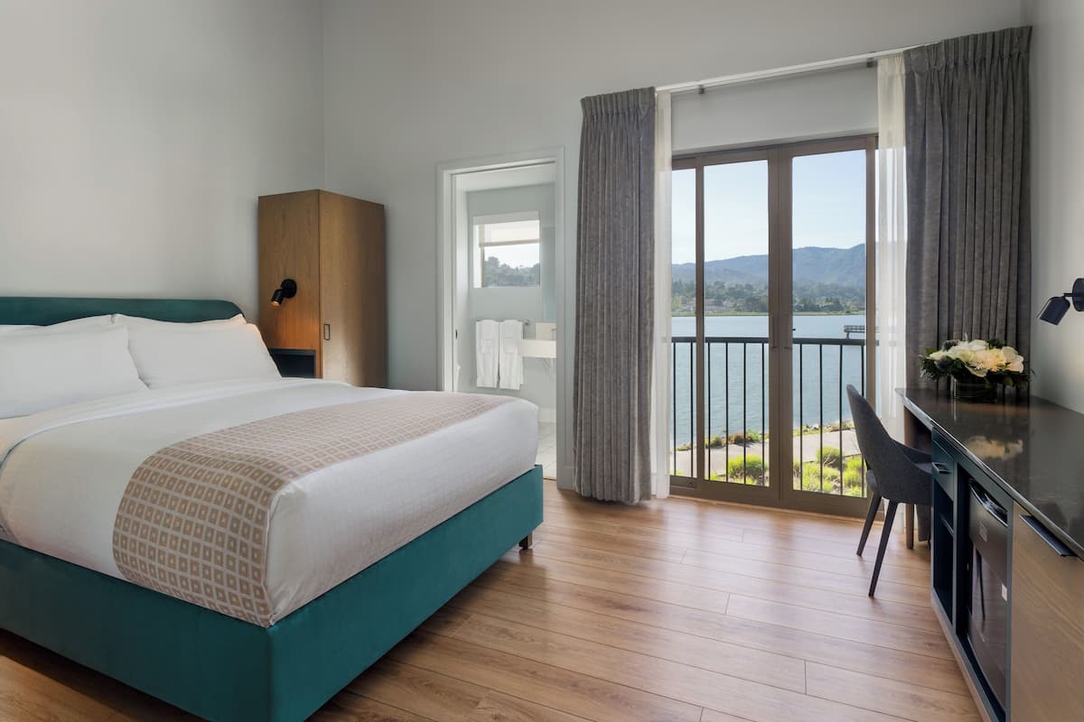 A hotel room with a bed, a desk, a chair, and a view of a lake.