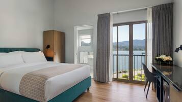 A hotel room with a bed, a desk, a chair, and a view of a lake.