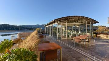 Enjoy breathtaking views of the water and distant hills from this outdoor terrace, featuring a glass-enclosed structure and comfortable seating.