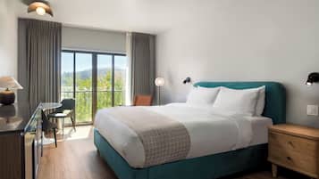 A hotel room with a large bed, a desk with a chair, a nightstand, and a view of the outdoors.