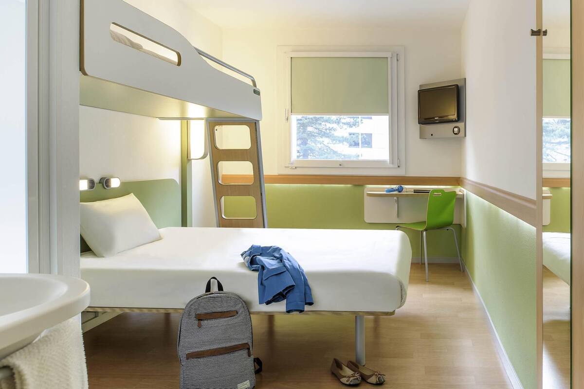 A compact hotel room with a bunk bed, a desk, a chair, a TV, and a bathroom.