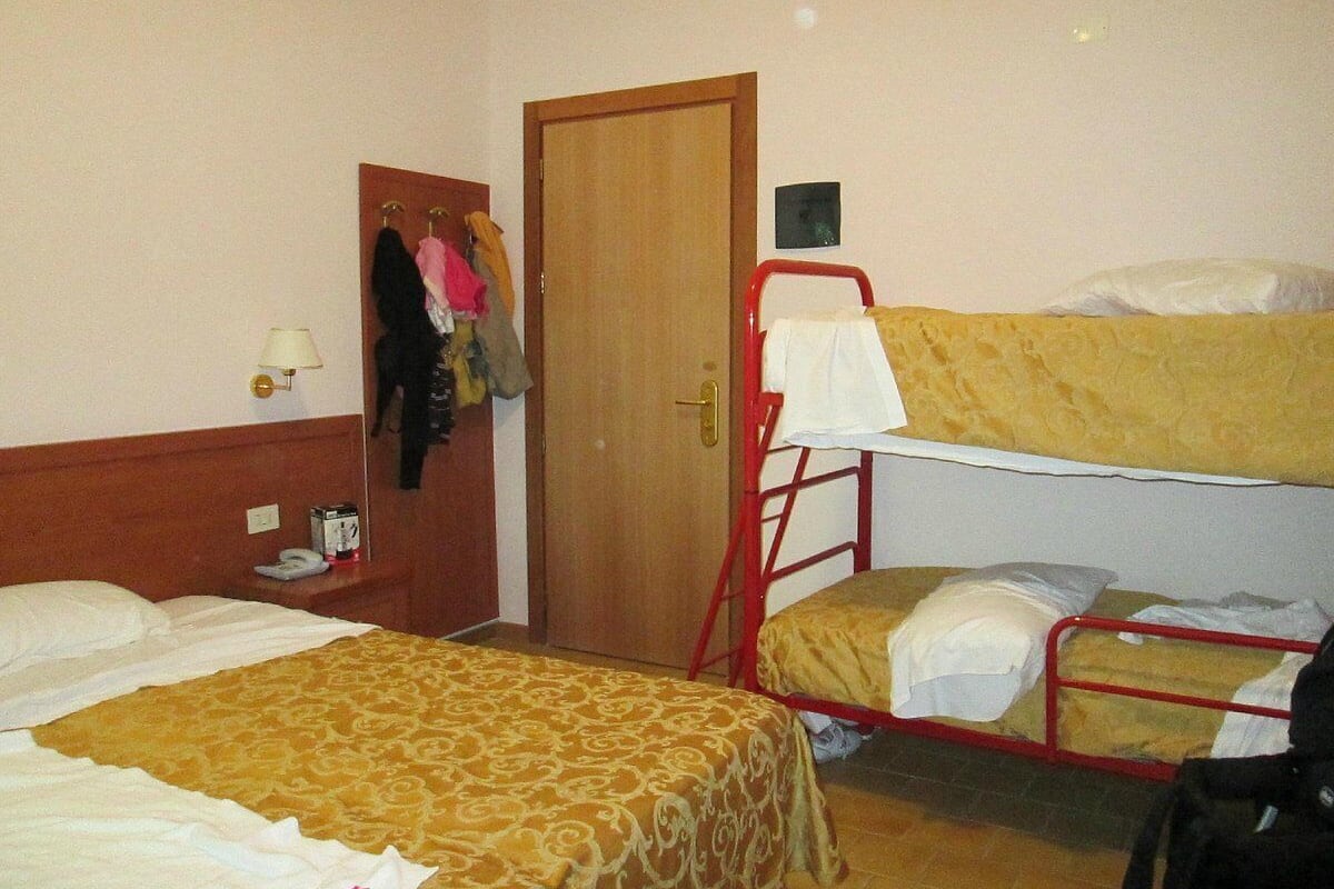 A hotel room with a single bed, a bunk bed, a wardrobe, and a small table with a lamp.