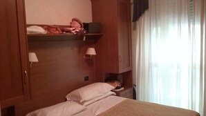 A hotel room with a bed, a nightstand, a lamp, a wardrobe, and a window with curtains. - Jole (Cesenatico)