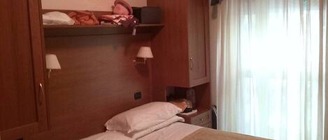 Une chambre d’hôtel avec un lit, une table de chevet, une lampe, une armoire et une fenêtre avec des rideaux.