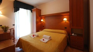 A hotel room with a bed, a desk, a chair, a wardrobe, and two bedside lamps. - Jole (Cesenatico)
