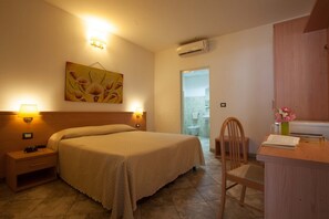 A hotel room with a bed, bedside lamps, a desk with a chair, a painting on the wall, and an air conditioning unit. - Camping Village Laguna Blu (Alghero)