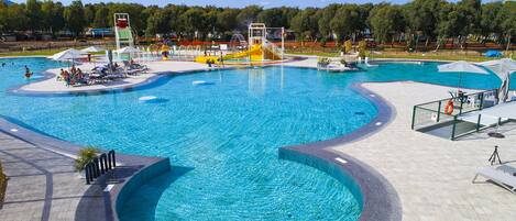A large outdoor swimming pool with multiple lanes and a water slide, surrounded by lounge chairs and umbrellas.