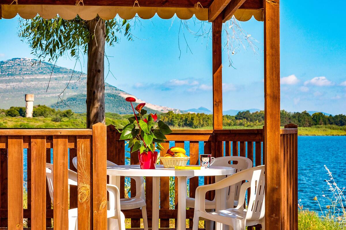A wooden deck with a table and chairs overlooking a lake, with a mountain in the background.