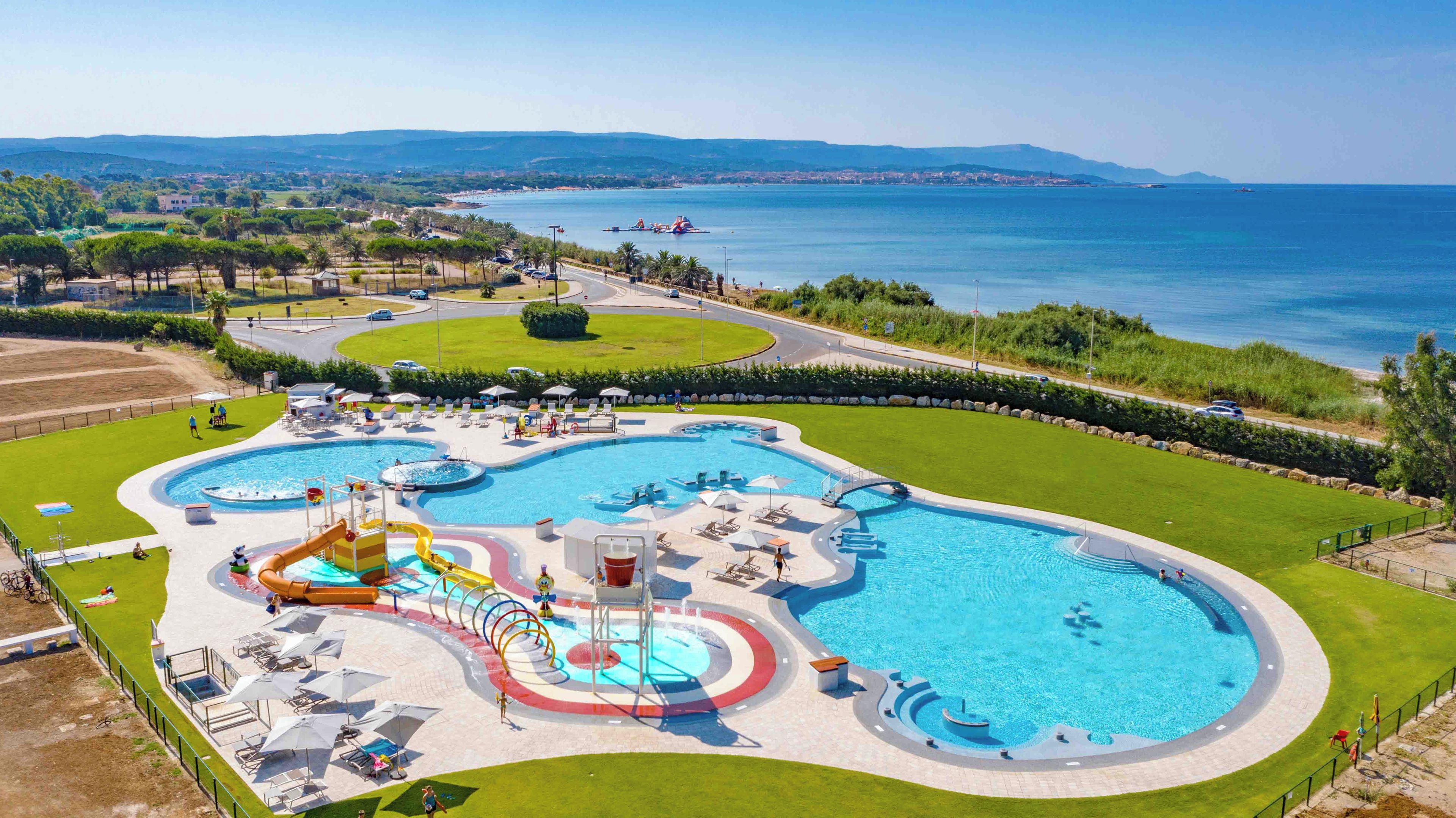 A large outdoor swimming pool with multiple water slides and a surrounding area with lounge chairs and umbrellas.