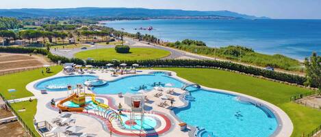 A large outdoor swimming pool with multiple water slides and a surrounding area with lounge chairs and umbrellas.