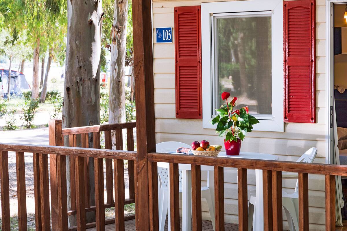 A wooden deck with a white chair and a table with a fruit basket and a vase of flowers.