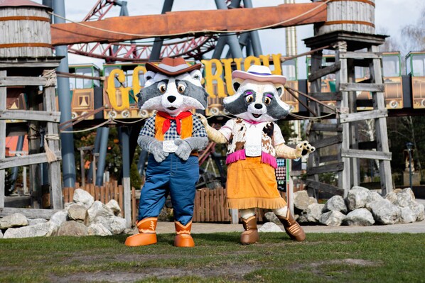 Two costumed characters standing in front of a wooden structure with a sign.