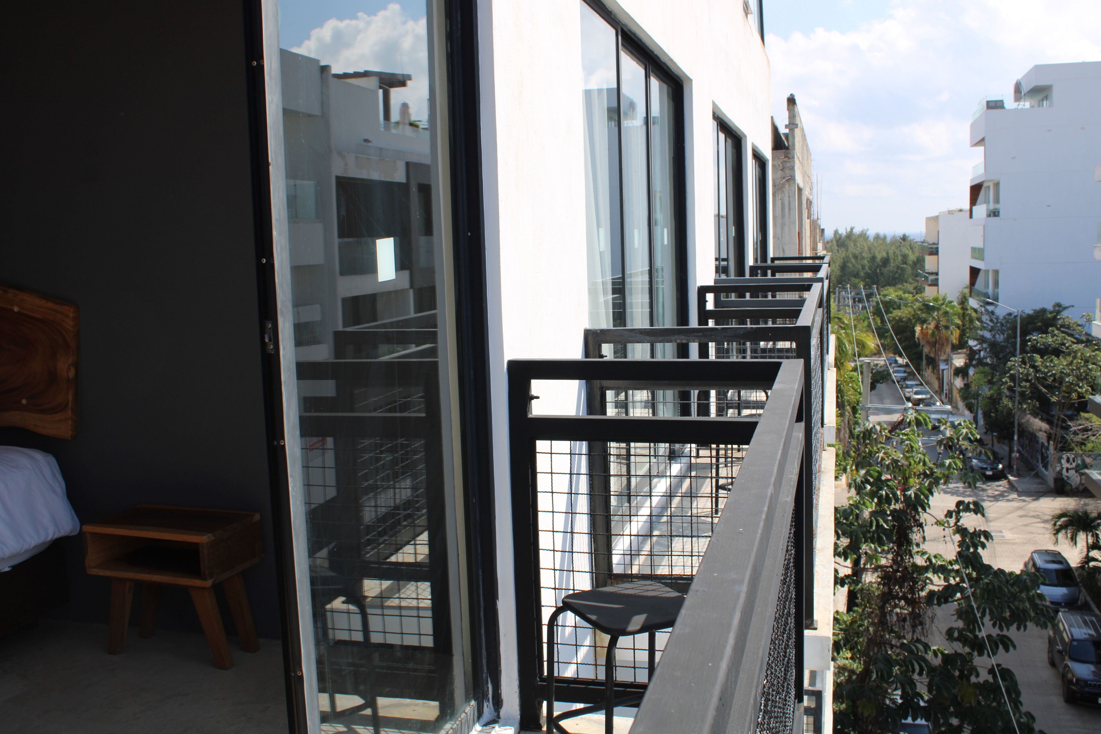 A balcony with a wooden bench and a chair, overlooking a street with parked cars and buildings.