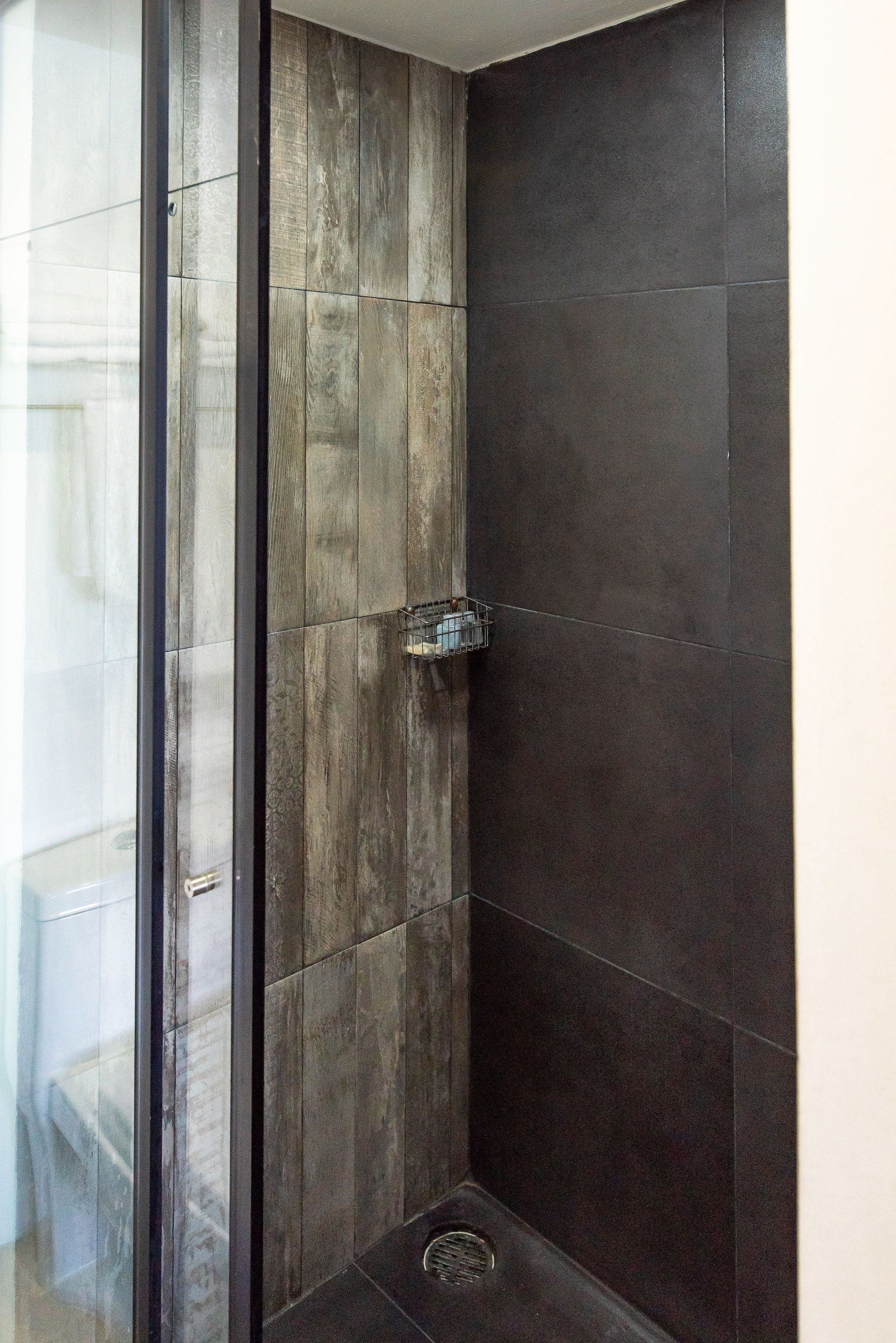 Ducha con azulejos oscuros y un diseño de paneles de madera.
