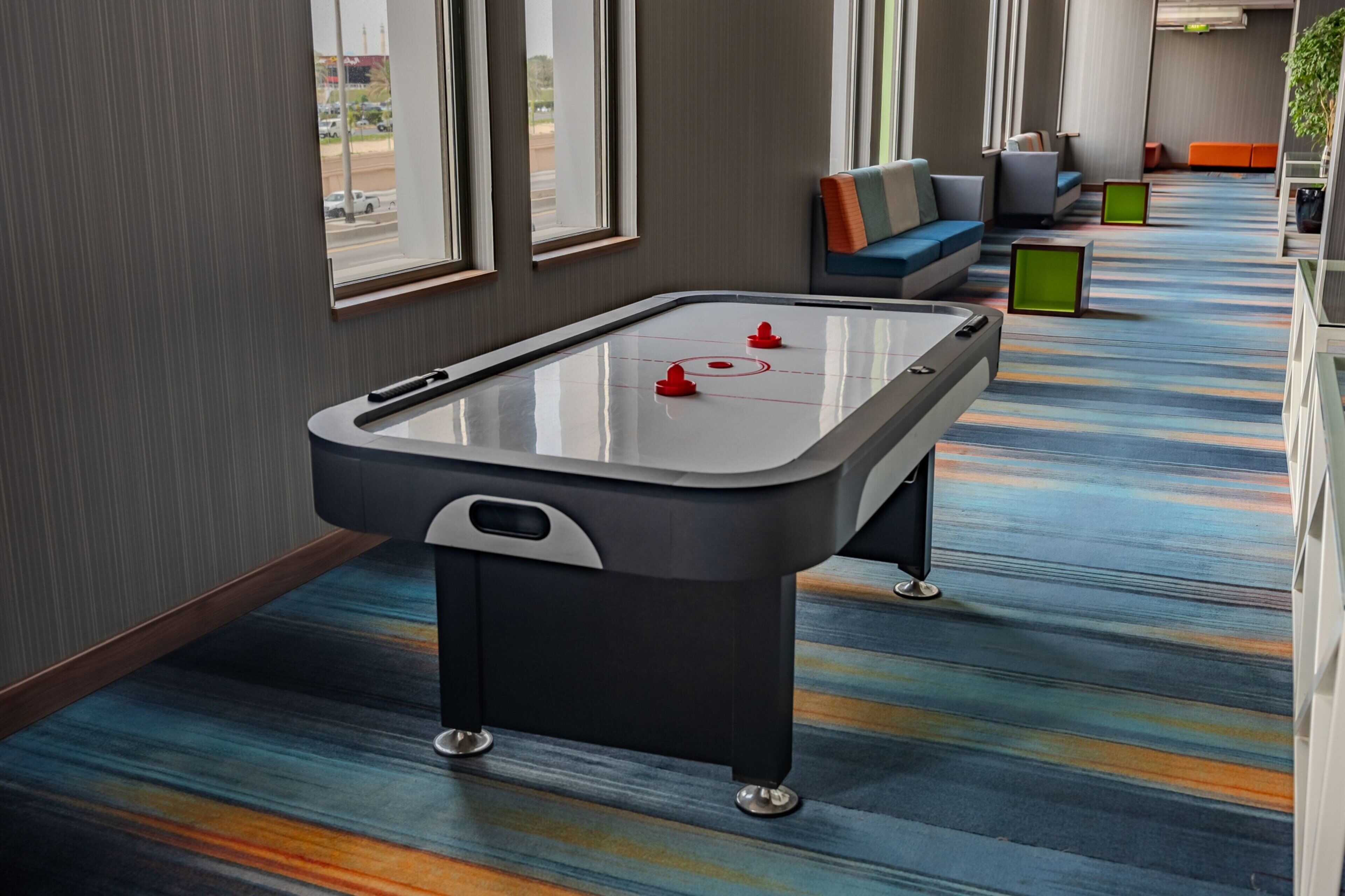 A pool table in a hotel lobby with a colorful striped carpet and seating area.