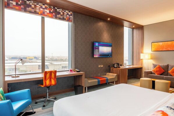 A modern hotel room with a large bed, a desk with a computer, a chair, a sofa, and a TV on the wall. - Aloft by Marriott Dhahran (Al Khobar)