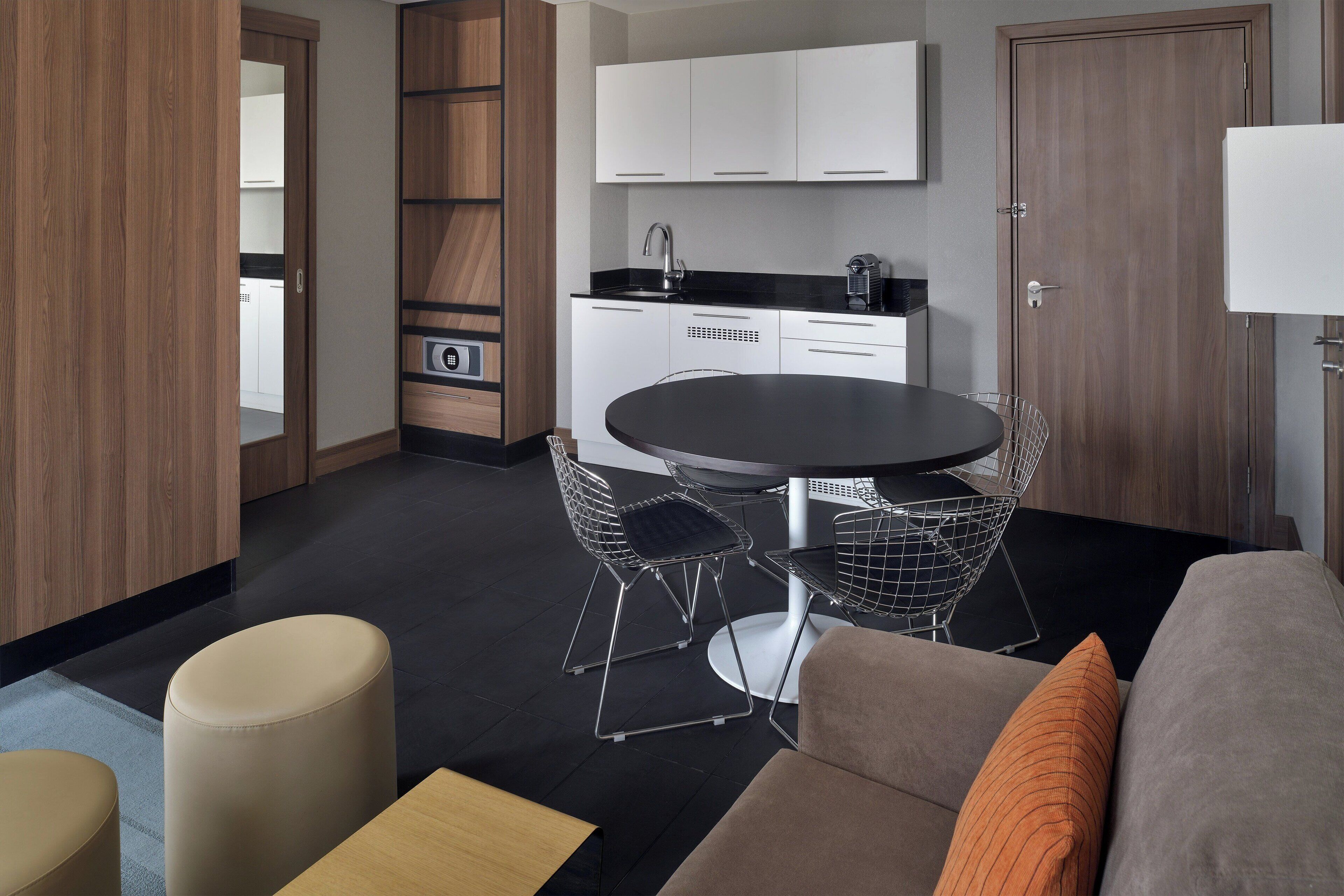 Una cocina moderna con armarios blancos, encimera negra y una mesa redonda con sillas de metal.