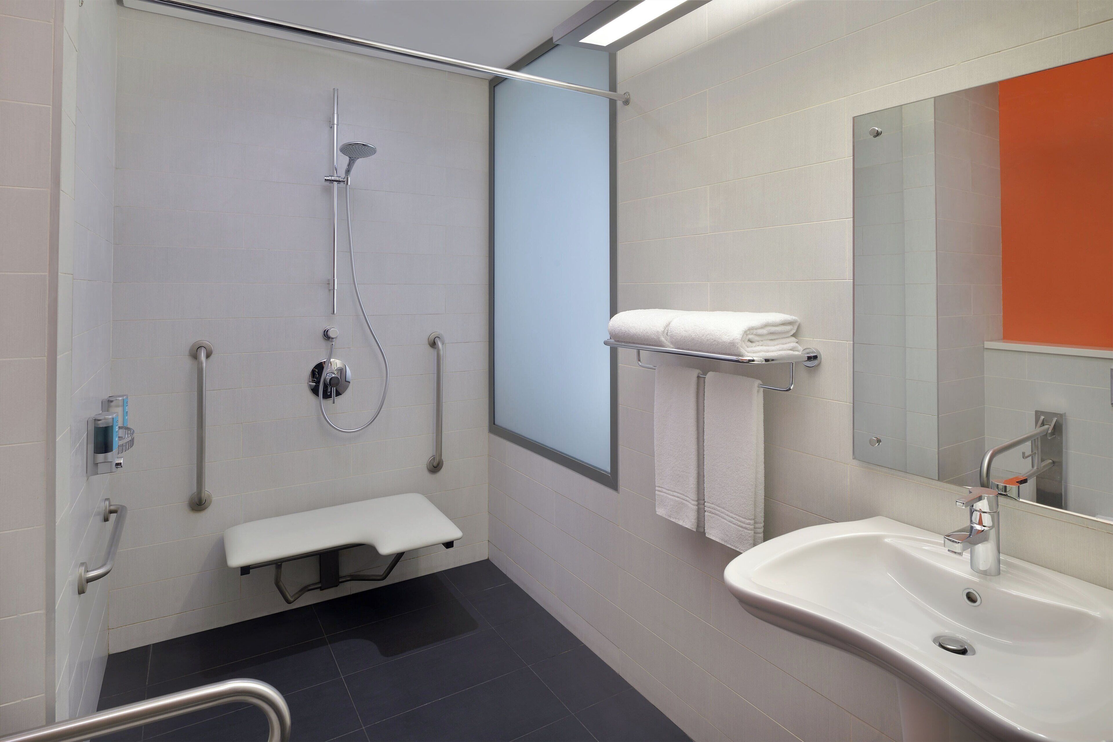 Ein modernes Badezimmer mit Dusche, Waschbecken, einer Bank und einem Handtuchhalter.