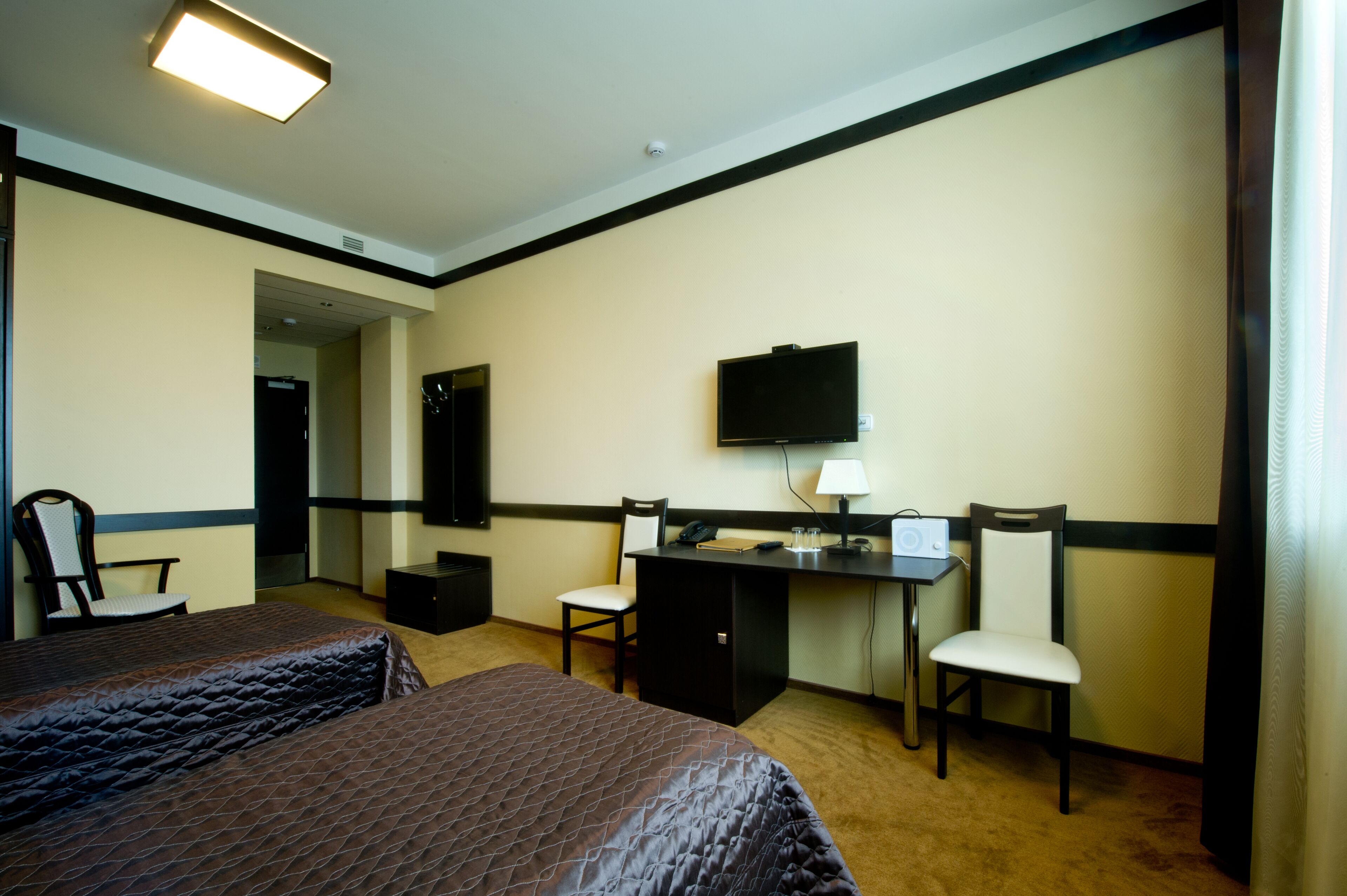 A hotel room with two beds, a desk, a chair, a television, and a lamp.