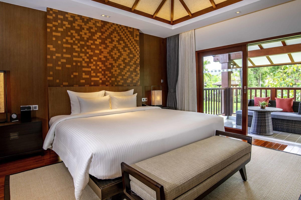 A large bed with white linens, a wooden headboard, and a bench at the foot of the bed.