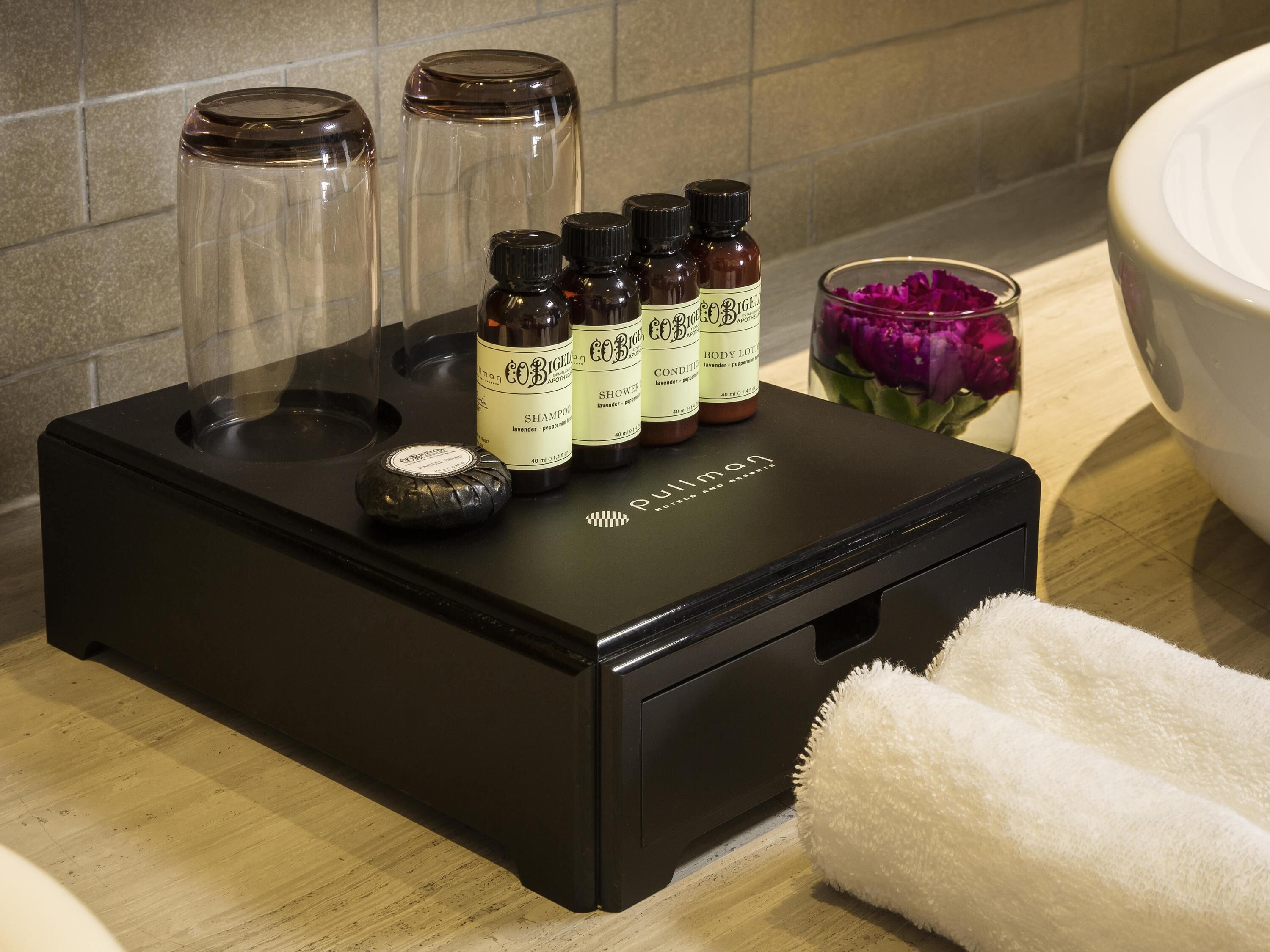 A black portable humidifier with three bottles of body lotion, a glass jar, and a white towel on a bathroom counter.