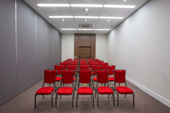 Un salón de conferencias con hileras de sillas rojas, una puerta de madera e iluminación empotrada en el techo.
